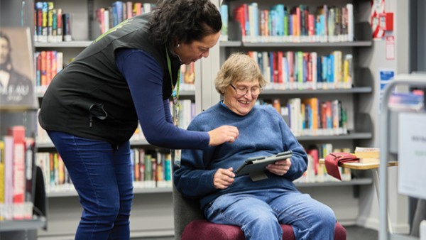 An older person with a tablet being assisted by a librarian.