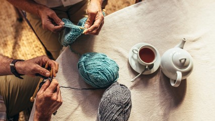 Two people knitting at a table with a pot and cup of tea.