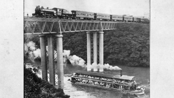 A train goes over the rail bridge at the same time as a steamer boat passes under the bridge on the Waikato River. 