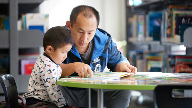 Man and child reading book at table
