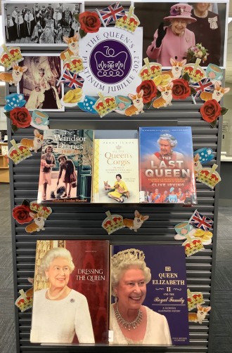 Book display at Glenview Library, featuring books and photos of the Queen, and illustrations of crowns, corgis, flags, and teacups.