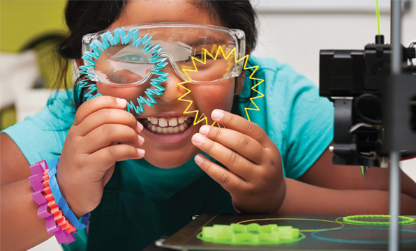 Smiling child wearing safety glasses and holding up 3D printed starburst shapes.